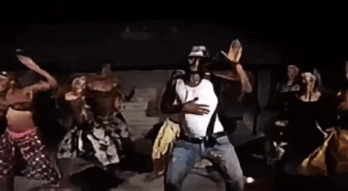 a man in a white tank top and hat is dancing in a dark room