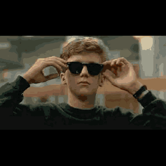 a young man wearing sunglasses and a black sweater is putting on his sunglasses .