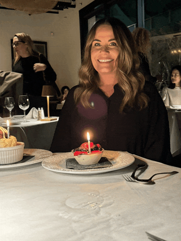 a woman sitting at a table with a candle on a plate of food