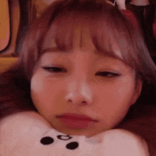 a close up of a woman 's face with a teddy bear pillow on her neck .