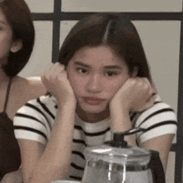 a woman in a striped shirt is sitting at a table with her hands on her face .