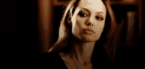 a close up of a woman 's face in a dark room with a bookshelf in the background .