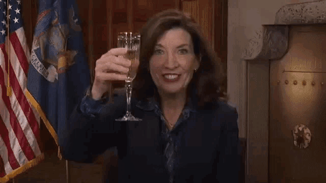 a woman is holding a glass of champagne in front of an american flag and cheering .