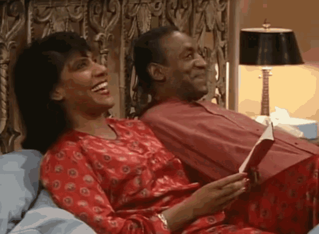 a man and a woman are laughing while sitting on a bed
