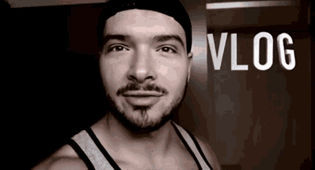 a man with a beard is wearing a beanie and a tank top with the word vlog written on the bottom