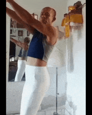 a bald man in a blue top and white pants is standing in front of a mirror