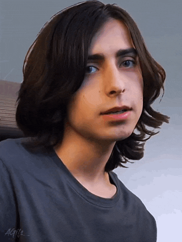 a young man with long hair is wearing a gray shirt with the letters agi 's on it