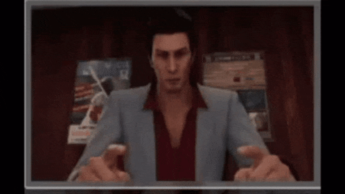 a man in a suit and red shirt is sitting in front of a television .