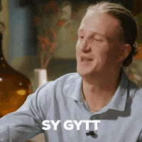 a man in a blue shirt is sitting at a table with the words sy gytt written on the bottom of his face .