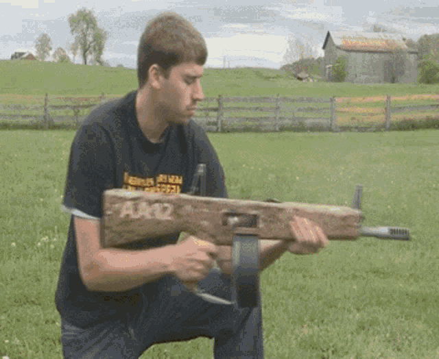 a man in a black shirt is kneeling down holding a wooden gun with the number aa12 on it
