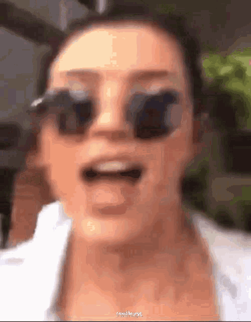 a close up of a woman wearing sunglasses and a white shirt .