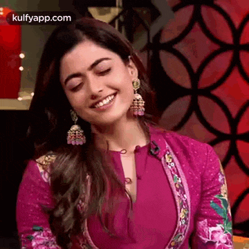 a woman in a pink dress is smiling with her eyes closed and wearing earrings .