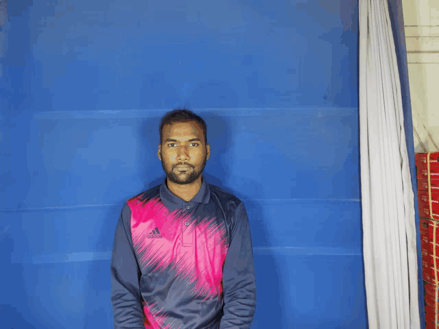 a man wearing a pink adidas shirt stands in front of a blue background