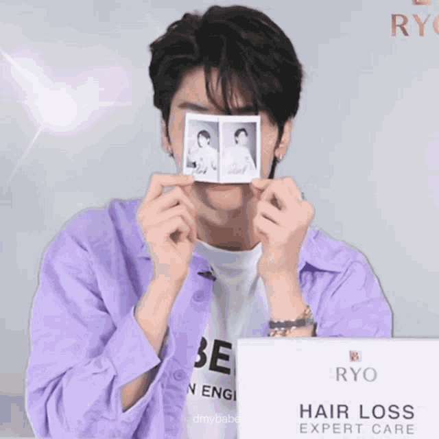 a man in a purple shirt is holding up a polaroid picture in front of his face