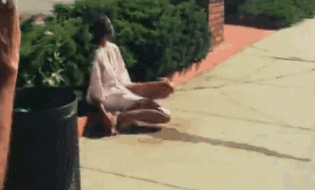 a woman in a white dress is sitting on the sidewalk next to a trash can .