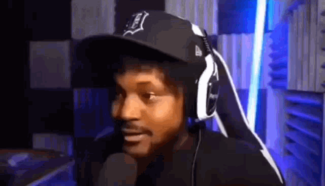 a man wearing headphones and a baseball cap is sitting in front of a microphone .