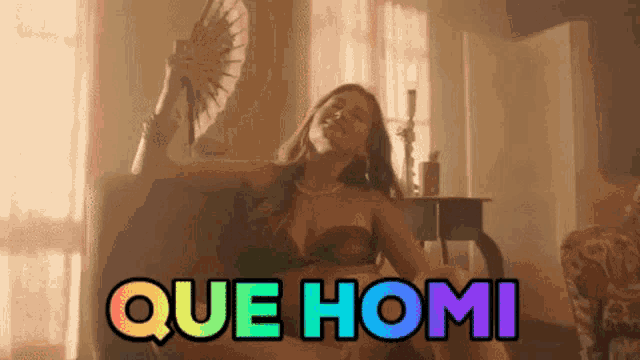 a woman is sitting on a couch holding a fan and the words que homi are displayed