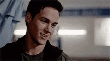 a young man is smiling and looking at the camera while sitting in a room .