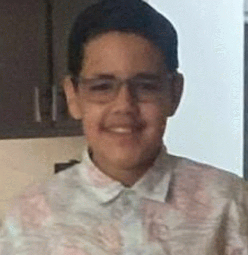 a young boy wearing glasses and a shirt is smiling at the camera .