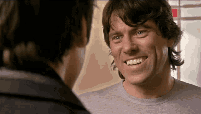 a man in a grey shirt is smiling and looking at another man