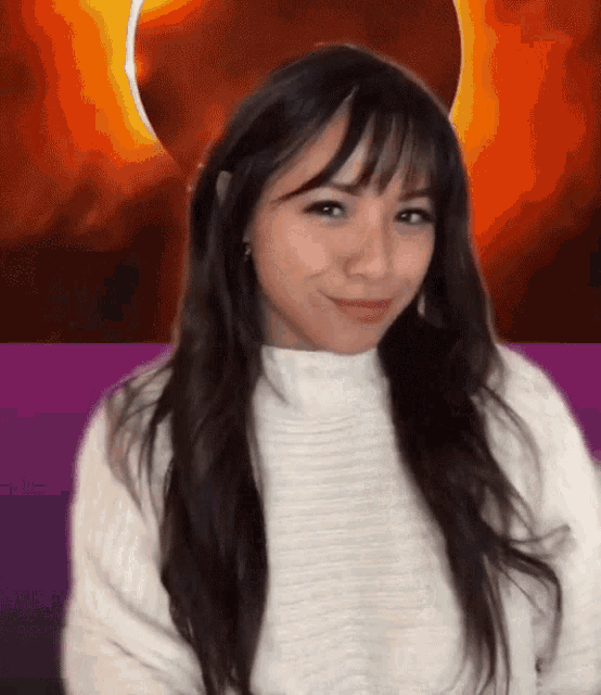 a woman in a white sweater is smiling in front of a purple background
