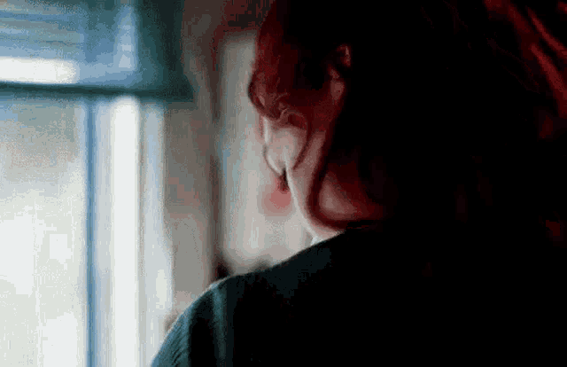 a woman with long red hair is looking out of a window .