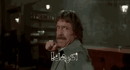 a man with a mustache is making a funny face and pointing at the camera in arabic .
