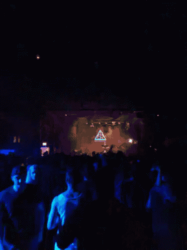 a crowd of people are dancing in a dark room with a blue light shining on a large k