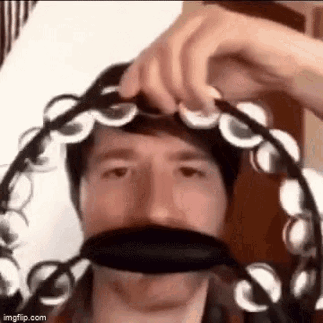a man is wearing a tambourine on his head and making a funny face .
