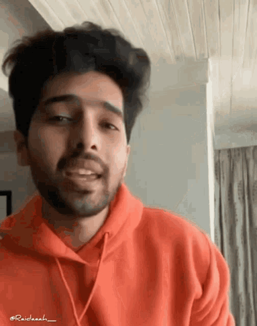 a man with a beard wears an orange hoodie