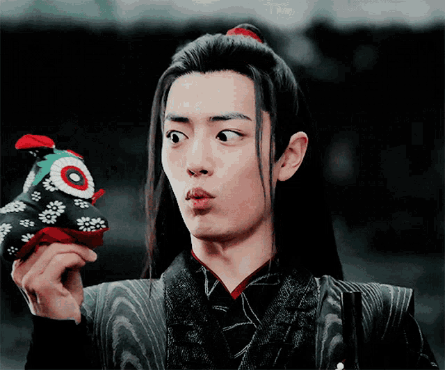 a man with long black hair is holding a stuffed animal in his hand
