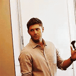 a man in a tan shirt is standing in front of a mirror holding a brush .