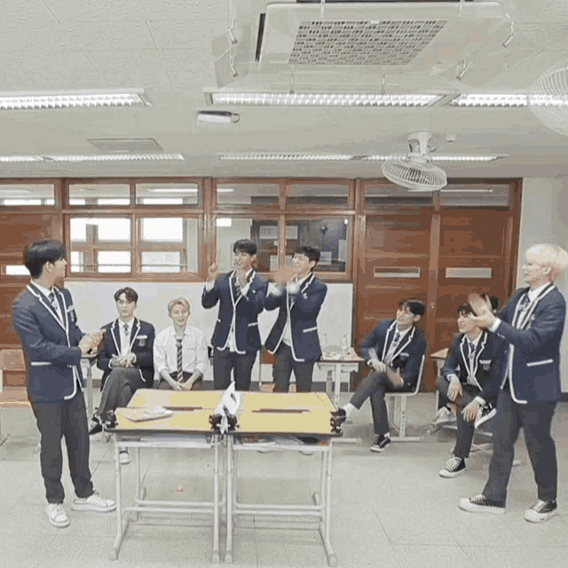 a group of young men in school uniforms are standing around a table