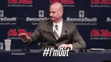 a man in a suit and tie is sitting at a table with microphones and says #i 'mout