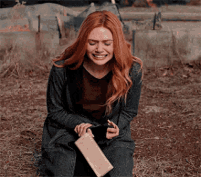 a woman with red hair is sitting on the ground holding a piece of paper and a cell phone .