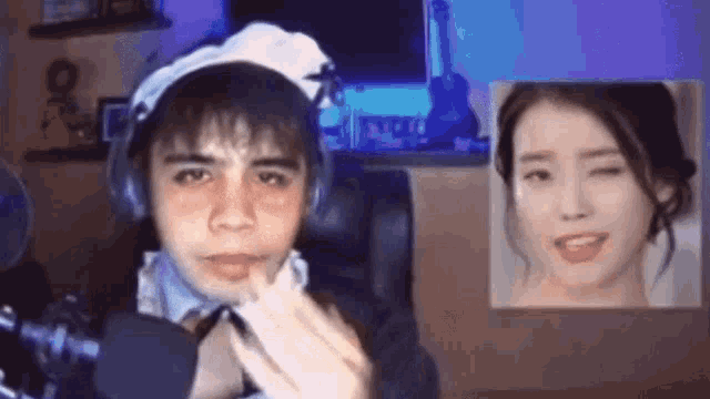 a man in a maid costume is talking into a microphone while a picture of a woman is behind him .