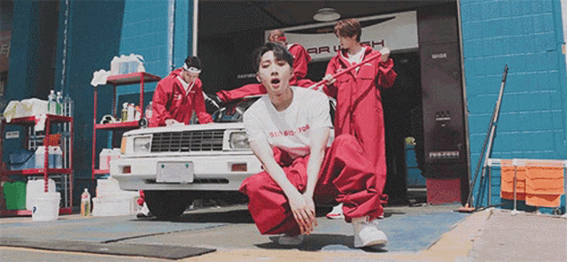a group of men in red jumpsuits are cleaning a car in front of a garage with a sign that says brush
