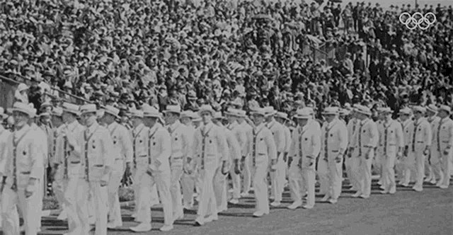 a black and white photo of a parade with the olympics logo in the corner