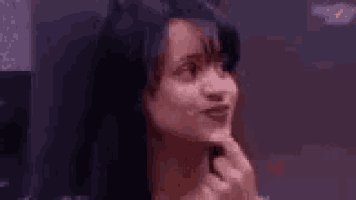 a woman with long black hair is holding her hand to her chin and making a funny face .