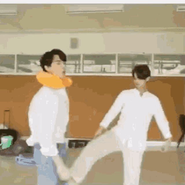 a couple of men are standing next to each other in a room and one of them is kicking the other 's leg .