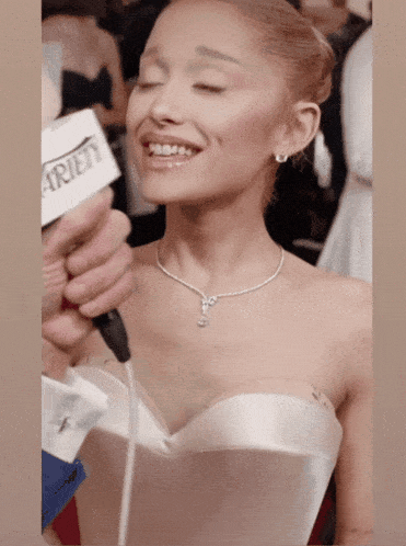 a woman in a strapless white dress is being interviewed by a man with a microphone that says variety on it