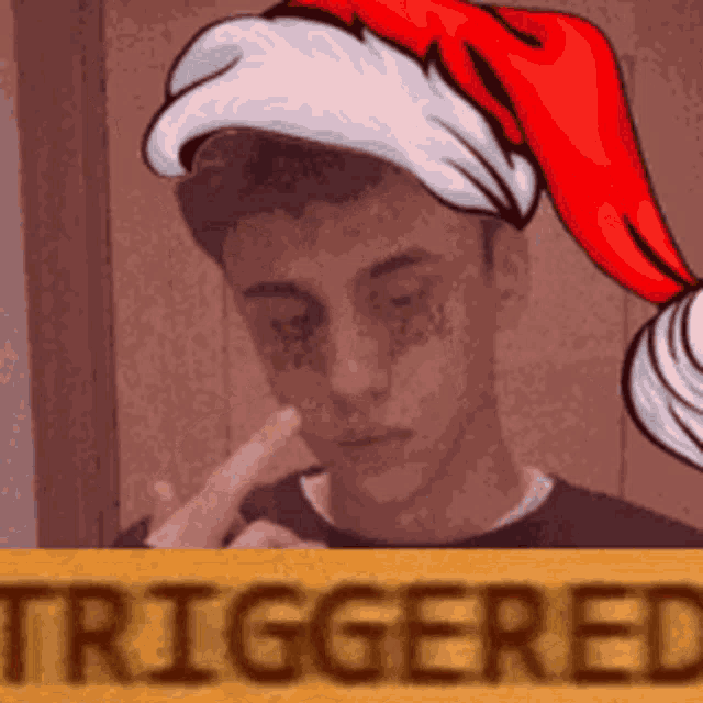 a young man wearing a santa hat is behind a sign that says triggered