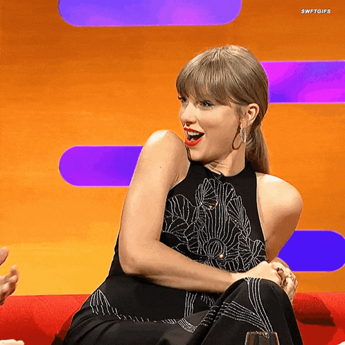 a woman in a black dress is sitting on a red couch with swiftgifs written on the bottom