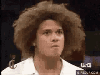 a man with a big afro looks at the camera while wearing a white shirt and glasses