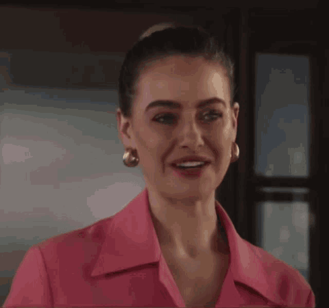 a woman in a pink shirt and earrings smiles