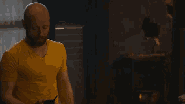 a bald man with a beard wearing a yellow shirt is holding a child in his arms .