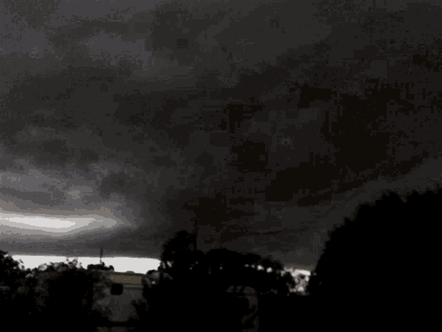 a black and white photo of a cloudy sky with trees in the foreground