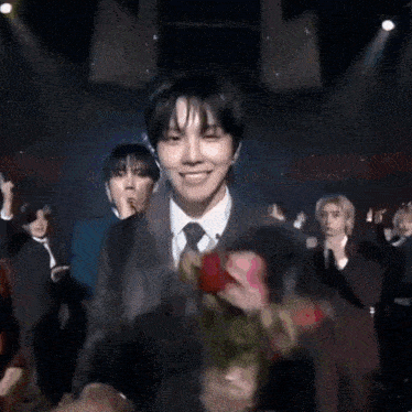 a man in a suit and tie is holding a bouquet of flowers in front of a crowd of people .
