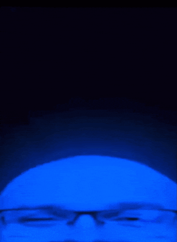 a man with glasses is smiling in a dark blue light