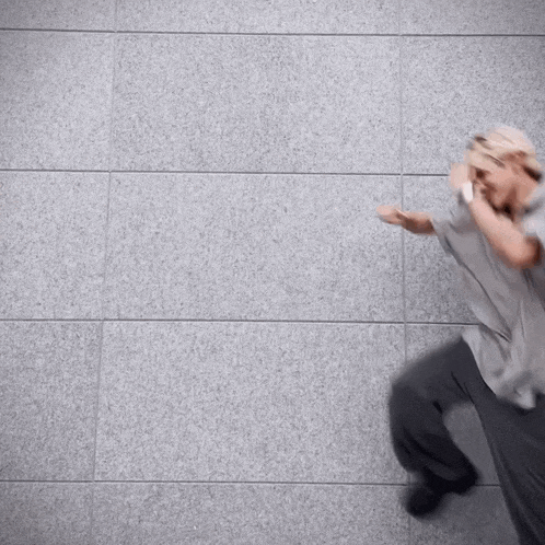 a man in a grey shirt and gray pants is standing in front of a gray wall